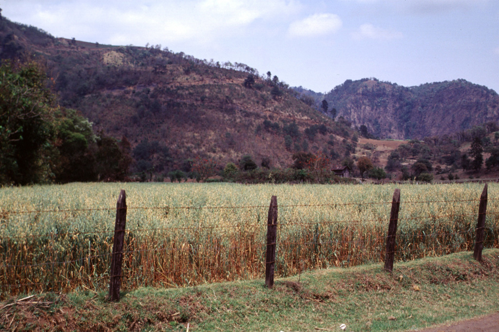 The Rincón de Chapultepec scoria cone is seen here with a switchback road on the southern flank and is one of the younger vents within the Naolinco volcanic field. The crater rim is barely visible against the tip of a ridge of the Sierra de Chiconquiaco range on which the cone was constructed. The valley floor is underlain by tephra deposits from Rincón de Chapultepec that overlie a lava flow that issued from the base of the cone. Rincón de Chapultepec formed about 3,000 years ago.  Photo by Lee Siebert, 2000 (Smithsonian Institution).