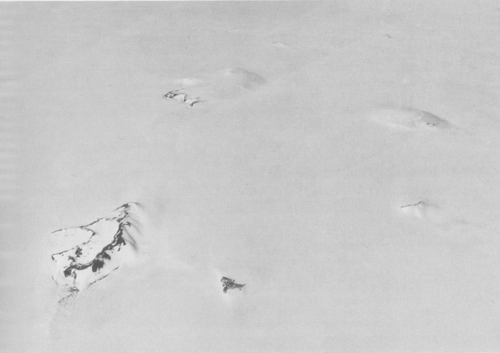 Hudson Mountains volcanic field comprises about 20 volcanic nunataks. These are peaks protruding from ice, and here represent the surface expression of multiple volcanic vents. At least four nunataks can be seen faintly in this image, looking across the southern Hudson Mountains from the west. The exposed ridge in the left foreground is Webber Nunatak. The uppermost, largely ice-covered nunatak seen here is Mount Manthe, one of the largest peaks in this volcanic field and dated to about 5 million years ago. A tephra layer from this field was erupted about 2,000 years ago. U. S. Navy photo TMA 2035 F31 203.