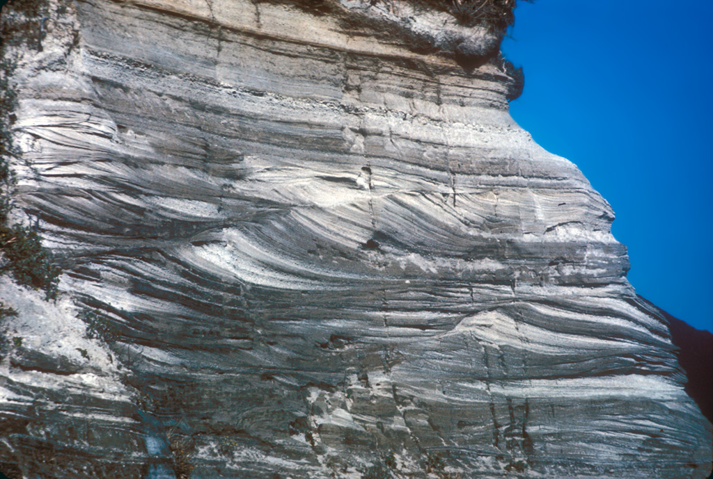 A sequence of pyroclastic surge deposits exposed in a sea cliff on Niijima, in the northern part of the Izu Islands of Japan. These cross-bedded layers were produced during repeated erosion and deposition by multiple pyroclastic surge events. The eruptions accompanied the formation of a lava dome at Mukaijima on the southern part of the island. The flat airfall deposits cap the exposure. Photo by R.V. Fisher, 1979 (University of California Santa Barbara).