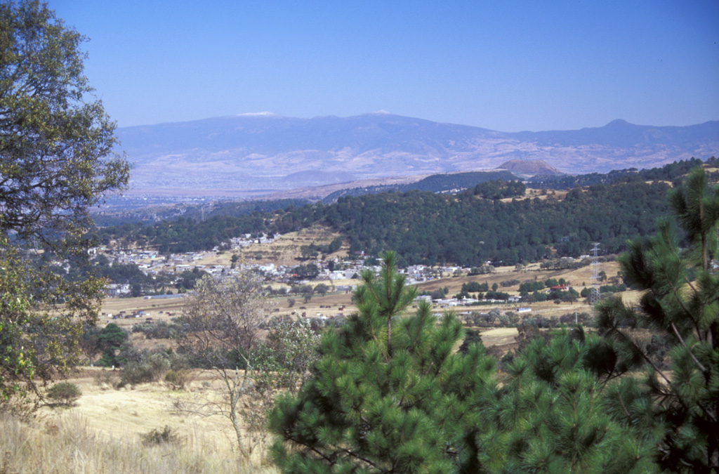 Papayo is the small rounded lava dome on the far-right horizon; the two peaks with snow-dusted summits on the horizon are Tláloc (left) and Telapón (center). This view looks to the NE across the Valley of Mexico from the flanks of the Chichinautzin range. Photo by Lee Siebert, 2004 (Smithsonian Institution).