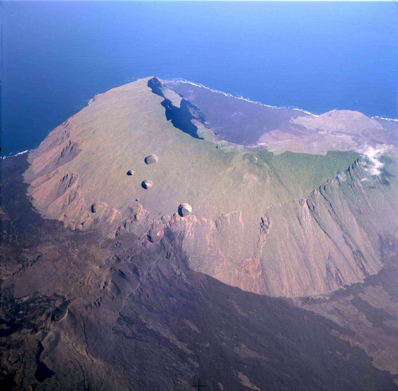 An aerial view from the NE shows Volcán Ecuador with its large caldera breached to the SW.  Erosion has extensively modified the lower outer flanks of the volcano.  East flank fissures at the lower left feed fresh lava flows, and large pit craters dot the upper eastern flank of the volcano.  A large pyroclastic cone constructed on the floor of the caldera can be seen near the coast at the upper right, and fresh lava flows blanket the caldera floor.  Photo by Patricio Ramon, 2004 (Instituto Geofisca, Escuela Politecnica Nacional).