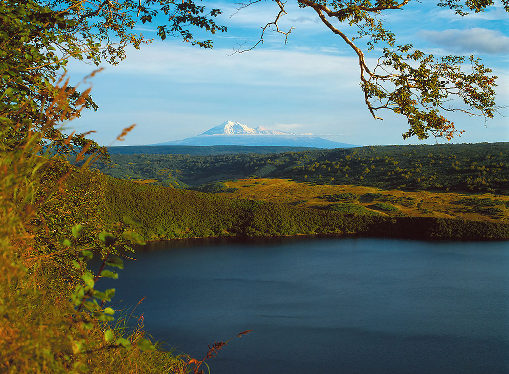 The Kinenin maar lies at the eastern foot of the Sredinny Range, about 80 km NW of Sheveluch seen in the background. The eruption took place about 1,100 years ago, and the maar is now partially filled by a 1-km-wide lake whose surface is at 400 m elevation. Copyrighted photo by Gennady Novikov, 2003 (Russian Academy of Sciences, Moscow).